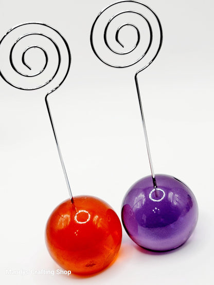 Two glass balls, one red and one purple, attached to metal spiral stands on a white background.