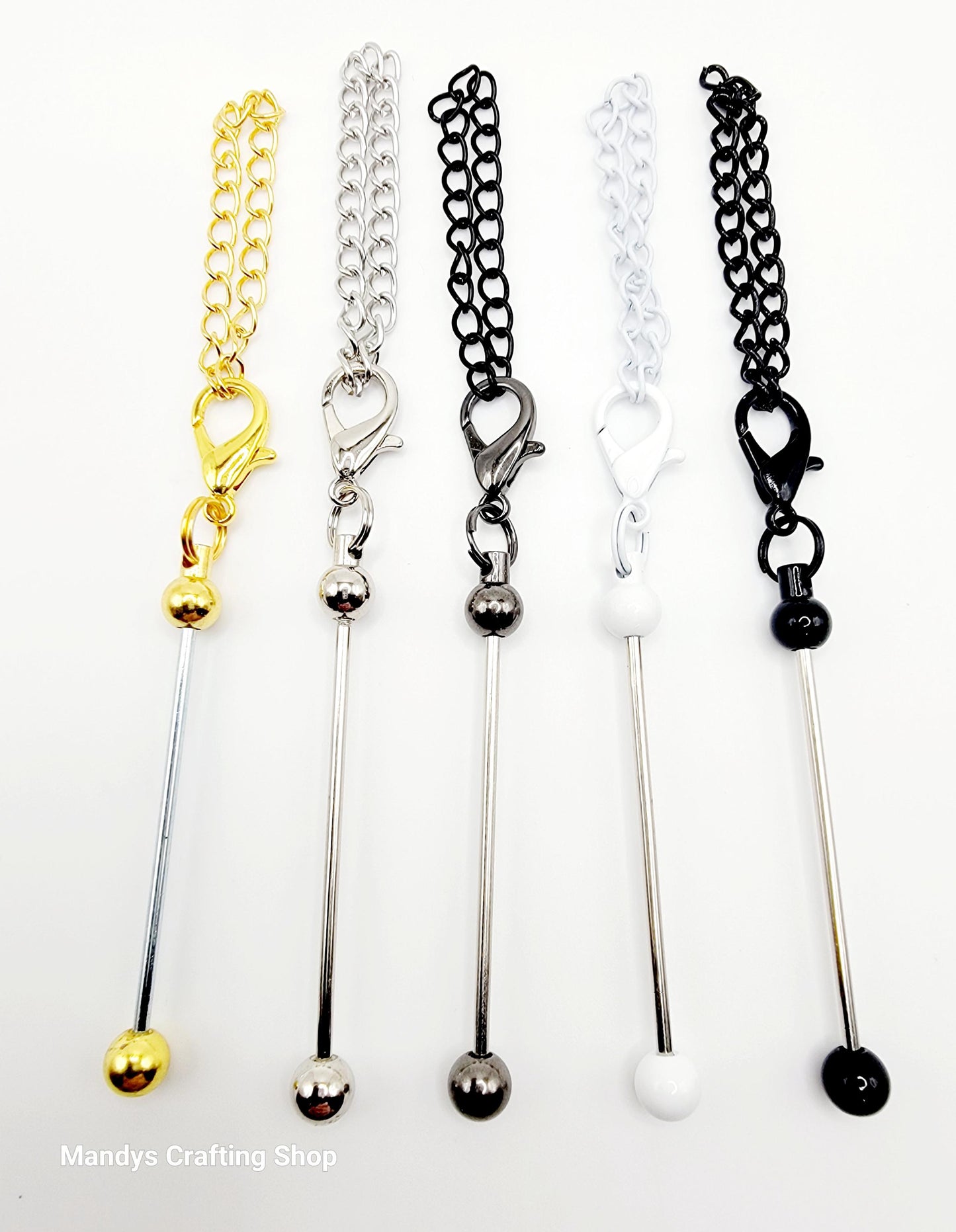 Set of five metal stir sticks with chain extensions in gold, silver, and black on a white background.