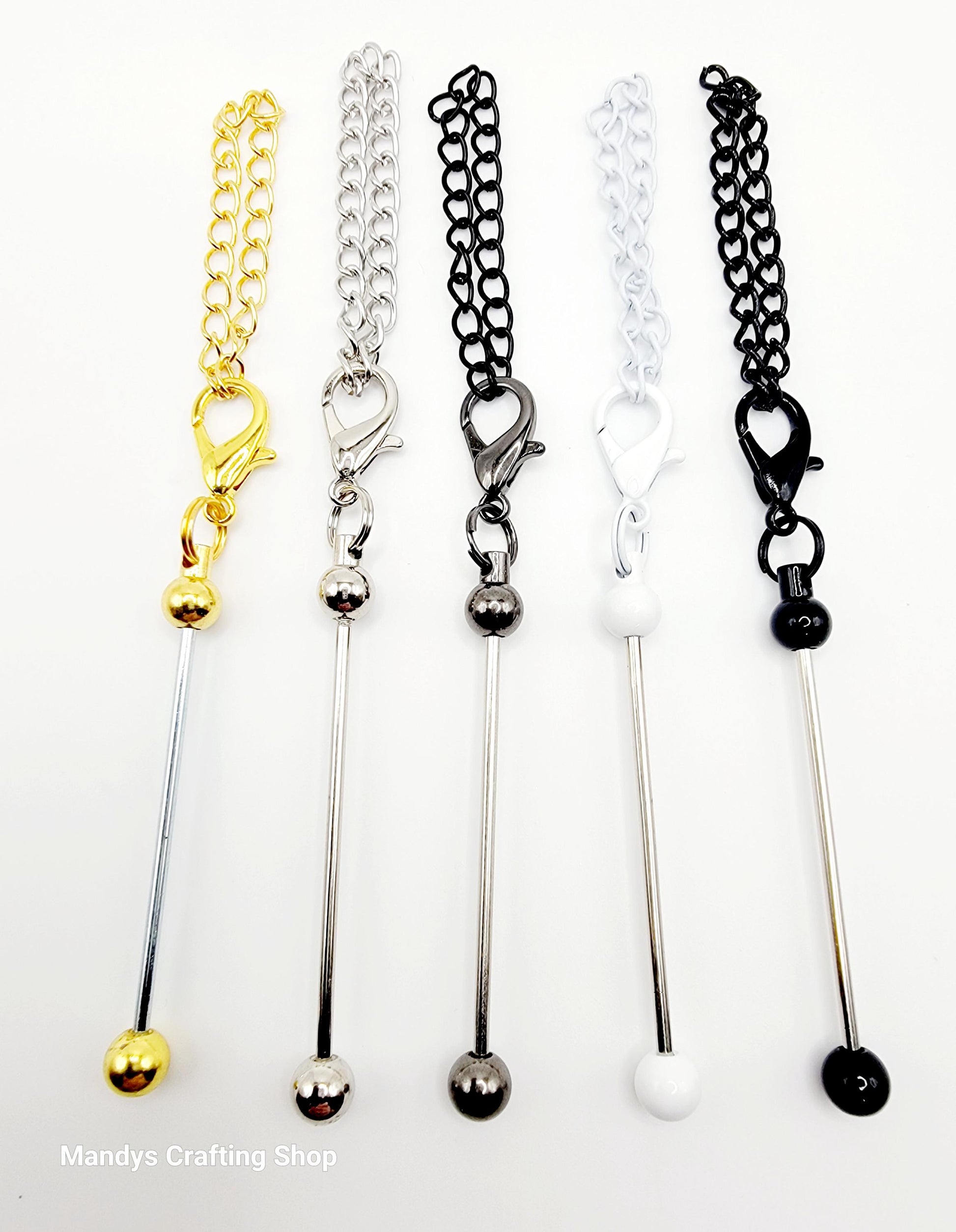 Set of five metal stir sticks with chain extensions in gold, silver, and black on a white background.