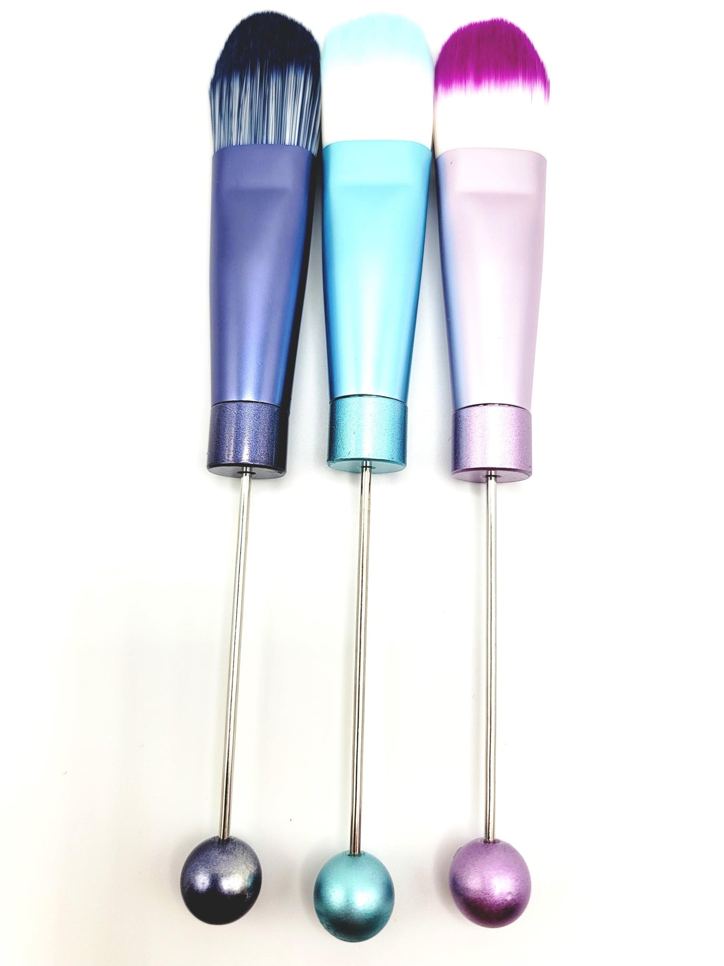 Three colorful makeup brushes with gradient handles on a white background