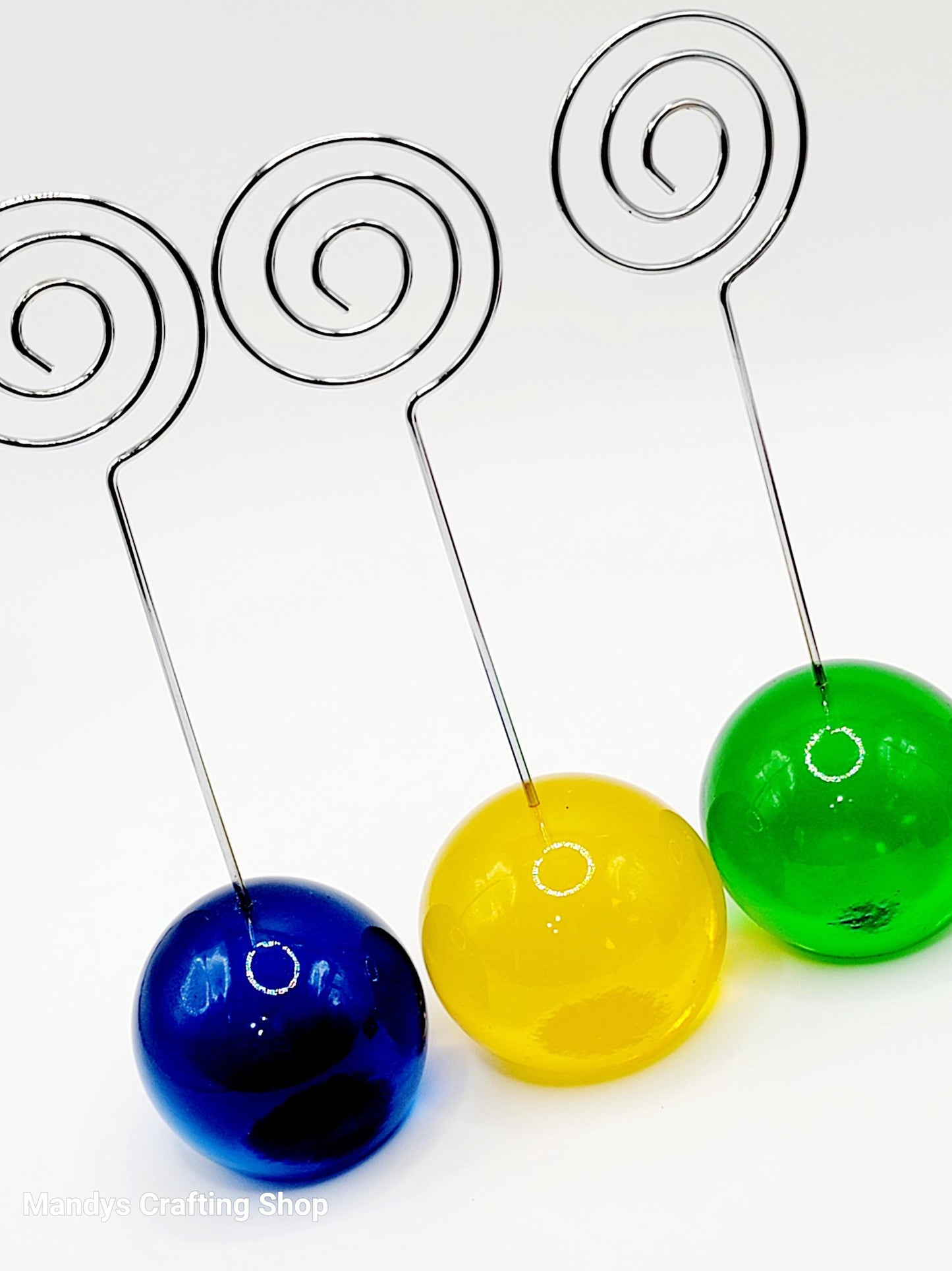 Three colorful glass beads on wire stands against a white background