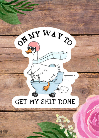 Cartoon duck on a toilet with text 'On my way to get my shit done' on a wooden background with flowers.